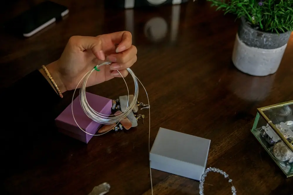 Hands bending jewellery wire with pliers at a work table